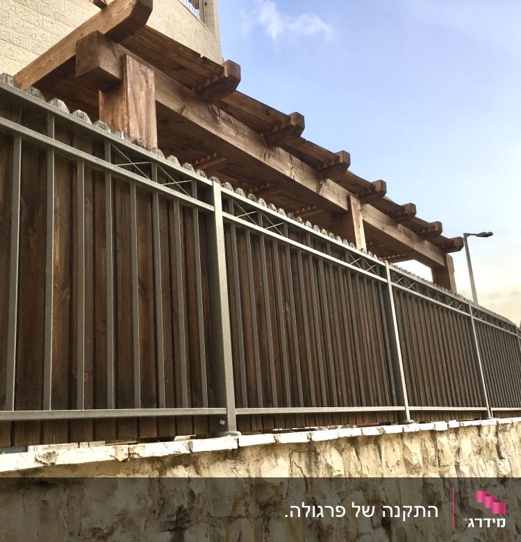 גדר עץ ומתכת על קיר אבן בגינה